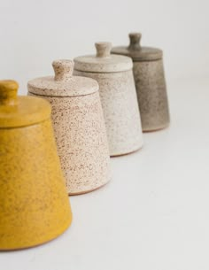 four different colored canisters lined up on a white surface with one yellow and the other gray