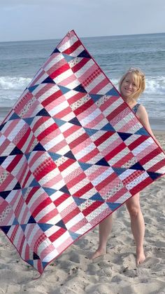 a woman on the beach holding up a red, white and blue quilt