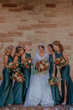 a group of women standing next to each other in front of a brick wall holding bouquets