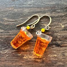 two cups of tea sitting on top of a wooden table next to earrings with yellow beads