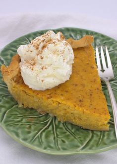 a slice of pumpkin pie on a green plate with whipped cream and a fork next to it