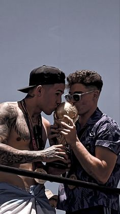 two men standing next to each other with tattoos on their body and one holding an object in his hand