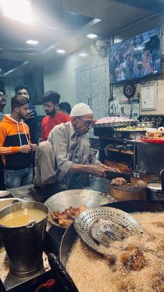 a group of people standing in a kitchen preparing food on top of pans and frying them