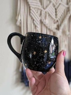 a hand holding a black coffee cup with stars and a unicorn on the inside, in front of a wall hanging