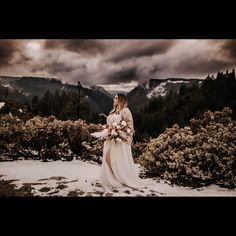 a woman standing on top of a snow covered slope holding a bouquet of white flowers