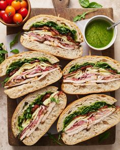 several sandwiches with meats and vegetables on a table next to some sauce in a bowl