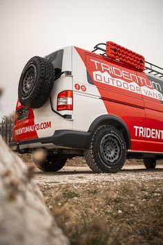 a red and white van parked on top of a dirt field