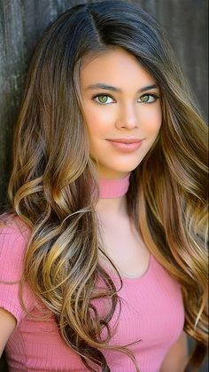 a beautiful young woman with long brown hair posing for a photo in front of a wooden wall