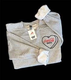 Indulge your soda obsession with our exclusive embroidered crewneck (or T-SHIRT) featuring the iconic Coke Zero logo! Crafted with meticulous attention to detail, this cozy crewneck is a must-have for any soda enthusiast. Available in sizes small to 2XL and offered in two stylish colors, Sports Grey, Sand or Crispy White, it's the perfect addition to your casual wardrobe. Whether you're lounging at home or hitting the town, this crewneck is sure to turn heads and spark conversations among fellow Casual Crew Neck T-shirt With Custom Embroidery, Trendy Custom Embroidery Tops For Streetwear, Casual Tops With Custom Embroidery In Relaxed Fit, Casual Tops With Custom Embroidery And Relaxed Fit, Casual Embroidered Crew T-shirt, Casual Short Sleeve Sweatshirt With Custom Embroidery, Zero Logo, Coca Cola Shirt, Trendy Embroidery