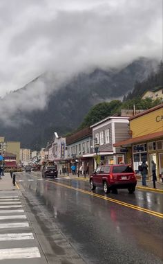 cars are driving down the street in front of buildings and mountains on a cloudy day