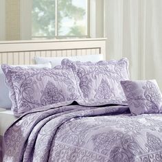 a bed with purple comforters and pillows on top of it in front of a window