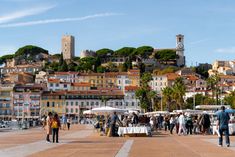 many people are walking around in front of some buildings and an old clock tower is on the hill behind them