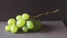 a bunch of green grapes sitting on top of a black countertop next to a branch