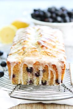 a blueberry loaf cake on a cooling rack with lemons and blueberries in the background