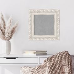 a white table topped with a vase filled with flowers next to a mirror and chair