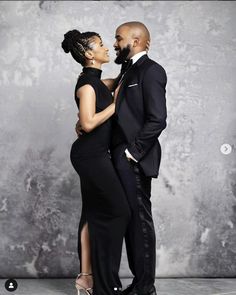 a man and woman standing next to each other in front of a gray wall wearing formal attire