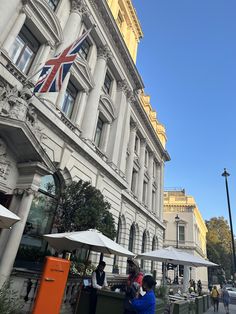 people sitting at tables in front of a building with an union jack flag on it