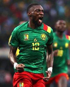 a soccer player in green and red is running with his mouth open while the other team mates look on