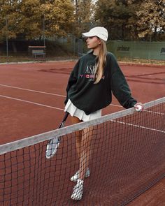 a woman holding a tennis racquet on top of a tennis court with trees in the background