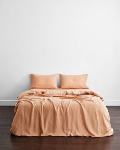 a bed with two pillows on top of it in front of a white wall and wooden floor