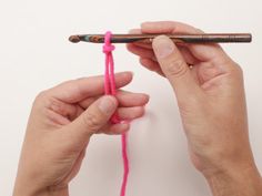 two hands are holding a crochet hook and knitting the hook with pink yarn