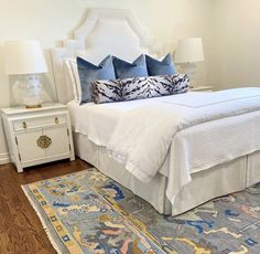 a bed with blue and white pillows on top of it next to a rug in a room