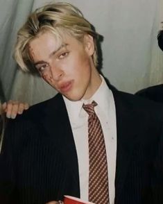 a young man in a suit and tie holding a red box with something on it