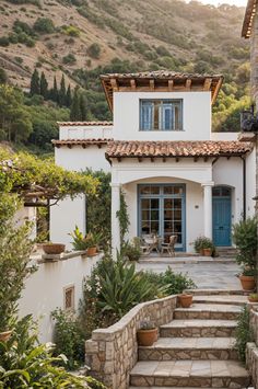 a white house with blue doors and steps leading up to the front door is surrounded by greenery