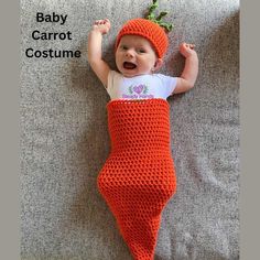 a baby laying on top of a couch wearing an orange crocheted blanket