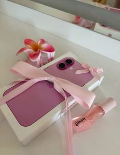 a pink cell phone in a white box with a pink ribbon on it and a bottle of lipstick next to it