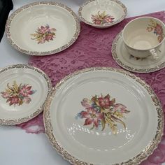 four plates with flowers on them are sitting on a pink table cloth next to a cup and saucer