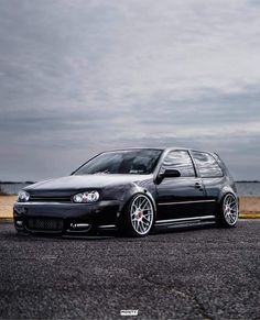 the black car is parked on the side of the road next to the water and clouds