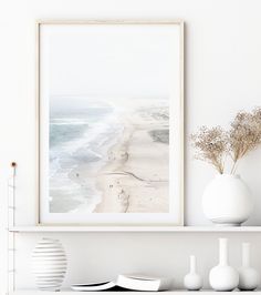 a white shelf with vases and books on it next to the ocean in front of a framed photograph