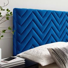 a blue headboard with two pillows and some books on the nightstand next to it