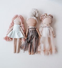 three dolls are sitting next to each other on a white surface, one is wearing a dress and the other has pink hair