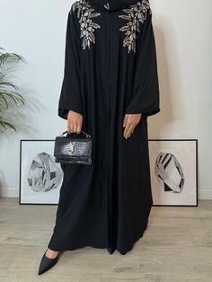 Introducing our Gold Floral Embroidered Open Abaya -- a pinnacle of luxury and refinement. Adorned with intricate floral embroidery, this timeless masterpiece features versatile pop-up buttons for effortless styling. Crafted from 100% Nida, it ensures comfort and durability, while the set includes a matching hijab and a complementary belt for a coordinated, polished look. Elevate your wardrobe with this symbol of opulence, machine washable for your convenience. Immerse yourself in authentic craf Elegant Black Embroidered Kimono, Embroidered Long Sleeve Agbada For Eid, Festive Black Embroidered Thobe, Long Embroidered Abaya For Eid, Black Abaya With Dabka Work For Eid, Traditional Black Embellished Abaya, Black Embroidered Abaya For Wedding, Black Embroidered Wedding Abaya, Wedding Black Embroidered Abaya