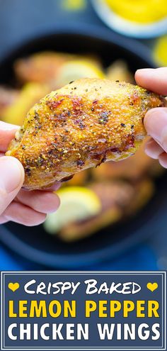 someone holding up a chicken wing in front of a skillet filled with lemon pepper chicken wings