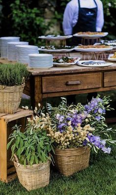 a table topped with lots of baskets filled with flowers next to a man in an apron