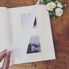 someone holding an open book with photos on it and flowers in the corner next to it