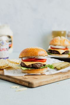 a cheeseburger with pickles and chips on a cutting board next to a bottle of ketchup