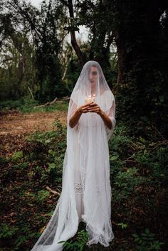 a woman wearing a veil and holding a candle in her hands while standing in the woods