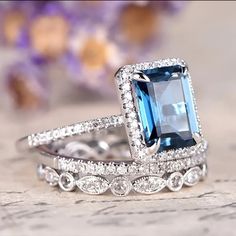 two wedding rings with an aqua blue stone surrounded by white gold and diamond accents, on top of a floral background