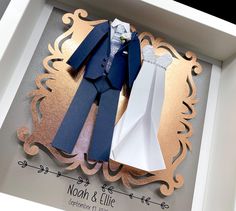 an origami wedding dress and tuxedo are displayed in a shadow box