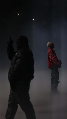 two people walking in the fog with one person wearing a red jacket and black pants