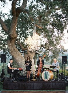 a group of people standing on top of a stage under a tree