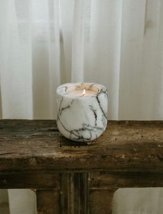 a marbled candle sitting on top of a wooden table next to a white curtain