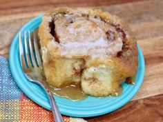 a blue plate topped with cinnamon roll covered in icing next to a knife and fork