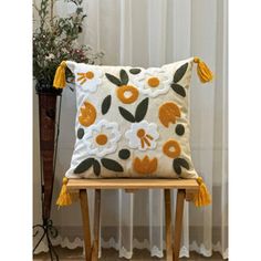 a white pillow with orange and yellow flowers on it sitting on a wooden chair in front of a window