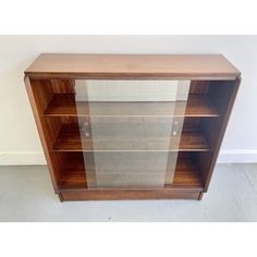 a wooden cabinet with glass doors on the top and bottom shelves, in front of a white wall