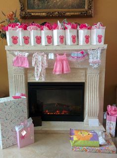 the fireplace is decorated with pink and white baby's clothes, gift bags, and presents